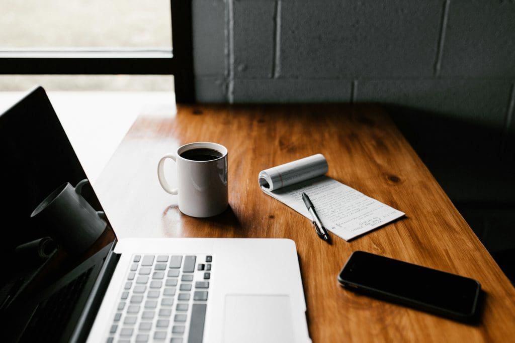 A desk with a laptop, coffee cup, cell phone, and notepad